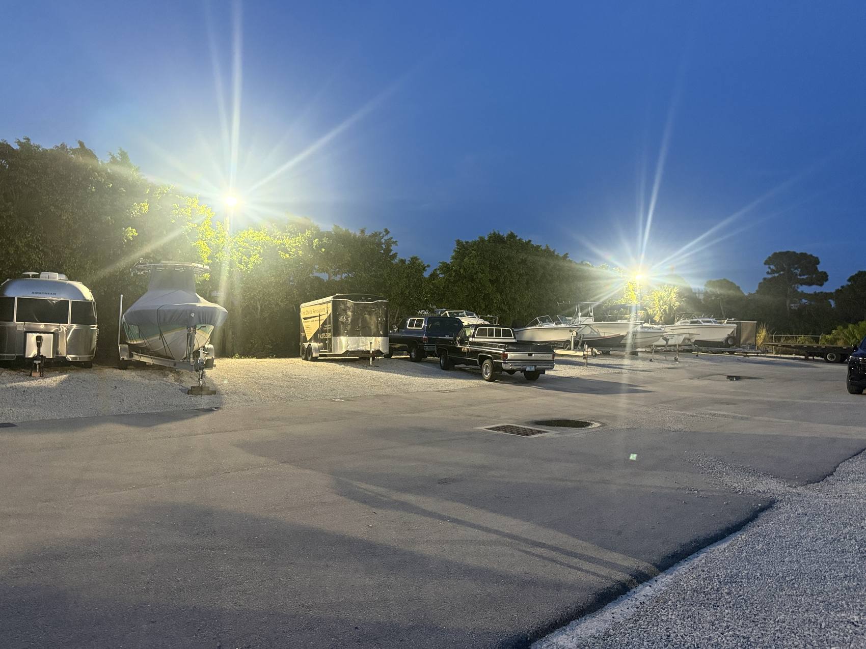 The Hypoluxo Dry Dock yard at dusk, pole lights burning over parked boats, trailers and trucks.