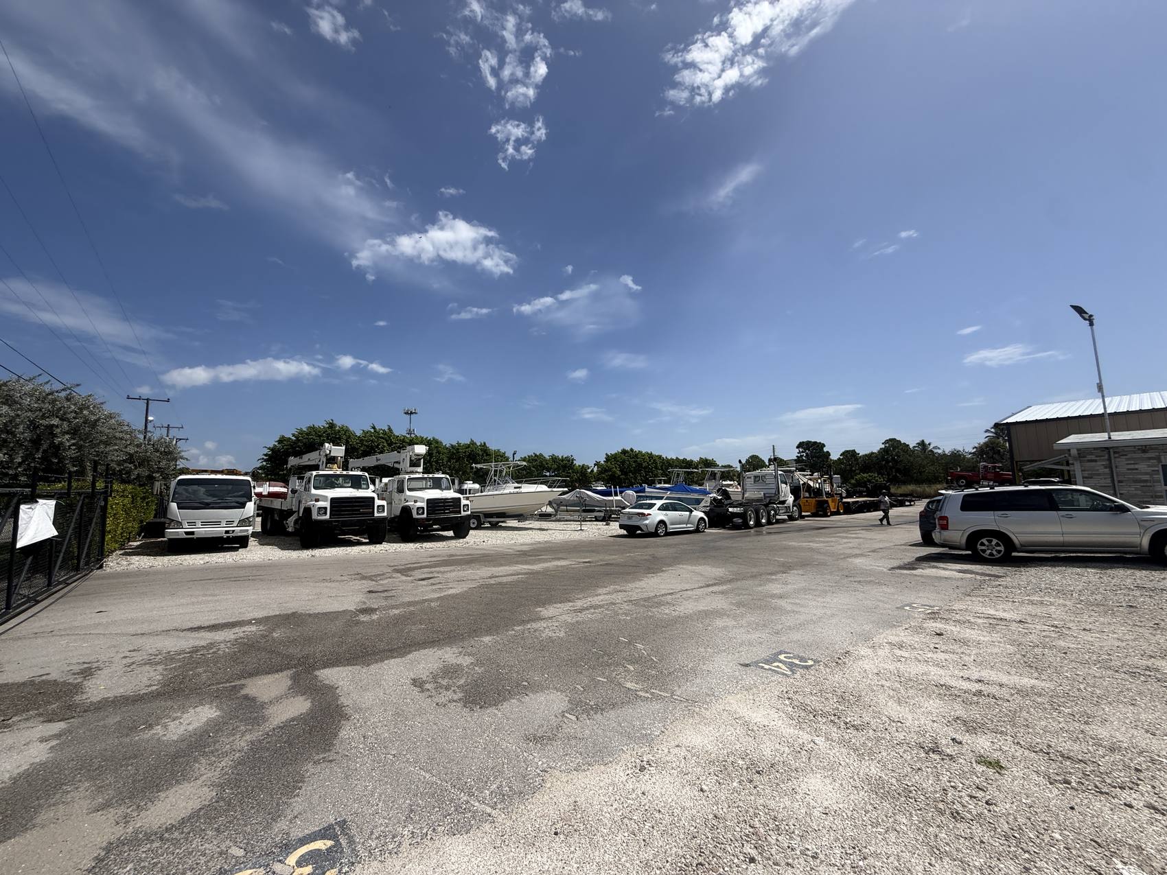 Wide view across the Hypoluxo Dry Dock yard: bucket trucks, boats on trailers, a numbered space painted on the asphalt, and staff on site.